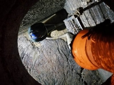 Wnętrze studzienki. Pracownik w kombinezonie naprawia kanalizację