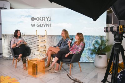 Studio Gdynia Filmowa, błękitne tło, trzy kobiety siedzą w fotelach i prowadzą rozmowę, między nimi przezroczysty stolik, dookoła sprzęt studyjny