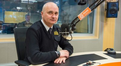 Janusz Walczak ubrany na czarno siedzi przy stole w studio radiowym.