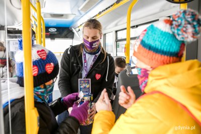 Wnętrze trolejbusu ZKM Gdynia, wolontariusz z puszką przyjmuje datki do puszki od dwóch osób