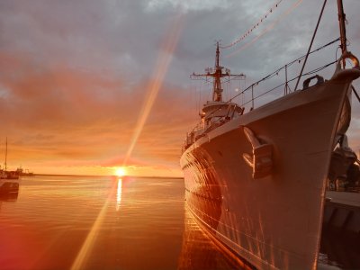 Okręt ORP Błyskawica zacumowany przy brzegu. Wschód słońca nad zatoką.