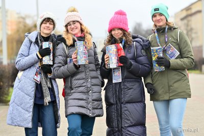 Cztery nastolatki w zimowych kurtkach, z puszkami WOŚP. Pozują do zdjęcia na skwerze Kościuszki