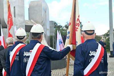 Poczet sztandarowy NSZZ „Solidarność” Stoczni Nauta przed pomnikiem Ofiar Grudnia '70 podczas uroczystości upamiętniających wydarzenia Sierpnia '80