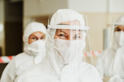 trójka medyków w białych kombinezonach covidowych, przyłbicach i maskach