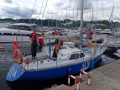 Pięć osób w kamizelkach na pokładzie jachtu szkoleniowego obok brzegu mariny w Gdyni