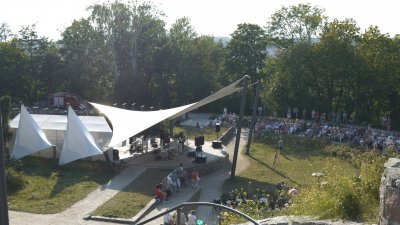 Grupa ludzi siedzi na koncercie w amfiteatrze na Kamiennej Górze. Na scenie muzycy