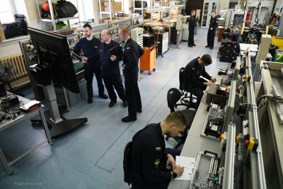 Pracownie techniczne AMW, aparatura, grupy studentów w granatowych uniformach, siedzą przy biurkach, stoją przy wyświetlaczu
