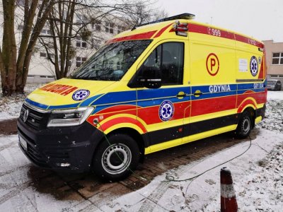 Żółty ambulans zaparkowany na placu, w tle śnieg