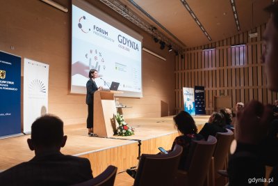Sala konferencyjna w PPNT. Na widowni publiczność. Na scenie Katarzyna Gruszecka-Spychała, przemawia przy katedrze. Na ekranie wyświetlony logotyp Forum Przedsiębiorstw