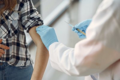 Zdjęcie ilustrujące szczepienie - osoba w białym fartuchu trzyma strzykawkę i robi zastrzyk kobiecie z podwiniętym rękawem