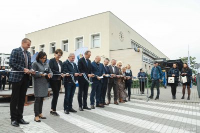 Dworzec PKP w Rumi, grupa osób przecina wstęgę, w tle budynek, namiot, ukłąd drogowy obok dworca
