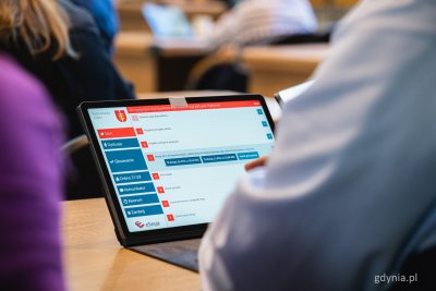 Sala obrad Rady Miasta, stół, widoczny jeden z radnych, na stole tablet z włączonym systemem głosowania