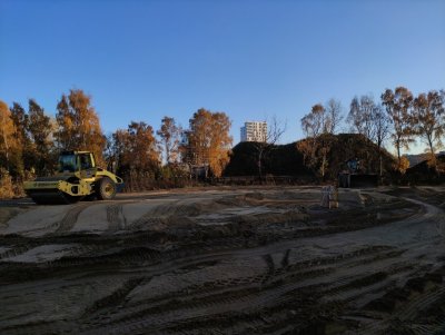 Plac budowy, ziemia. Koparka na placu, w tle budynki