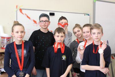 Grupa dzieci z drużyny Odysei z medalami na piersiach, jeden chłopiec trzyma medal w zębach. Fot. Sp nr 47.