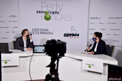 Stół studio telewizyjnego, przy stole Marek Tejchman i Agnieszka Janowicz. Trzymają mikrofony i rozmawiają. Na pierwszym planie kamera