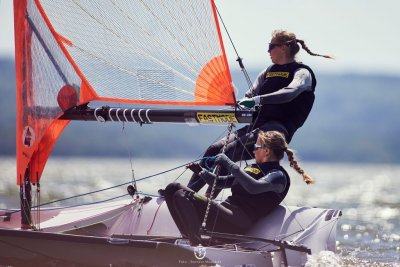 Dwie kobiety w piankach na pokładzie sportowego jachtu żaglowego, jedna trzyma za żagiel