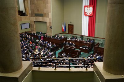 Sala sejmowa. Posłowie w ławach, obrady w trakcie. Widoczny sztandar biało-czerwony i filary z balkonu nad salą.