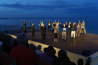 Scena zbiorowa w przedstawieniu „Marlena Dietrich. Iluzje”, którego pokaz zamknął 25. sezon Sceny Letniej. Na pierwszym planie siedząca na widowni publiczność. W tle morze // fot. Anna Rezulak