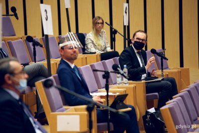 Na zdjęciu sala konferencyjna gdyńskiego PPNT. Drewniane siedziska z fioletowymi siedzeniami. Na zdjęciu Radni Miasta siedzący w odległości kilku krzeseł od siebie. Przy nich mikrofony na czarnych statywach. Trwa dyskusja.