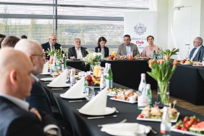 Sala konferencyjna. Kilkanaście osób przy stole, siedzą, na stole zastawa i żywność, w tle ścianka Business Centre Club, na środku Wojciech Szczurek i Katarzyna Gruszecka-Spychała