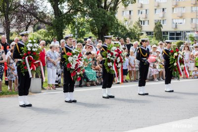 Marynarze trzymają biało czerwone wieńce, w tle mieszkańcy