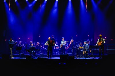 Oświetlona niebieskimi reflektorami scena. Na scenie zespół muzyczny, na pierwszym planie wyraźnie widoczny mężczyzna z akordeonem.