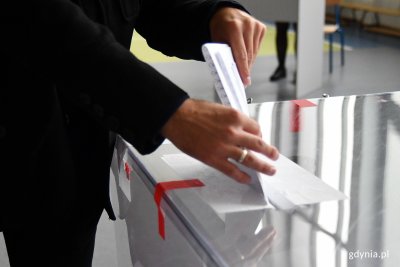 Osoba wrzucająca kartę do głosowania do urny w lokalu wyborczym w Gdyni