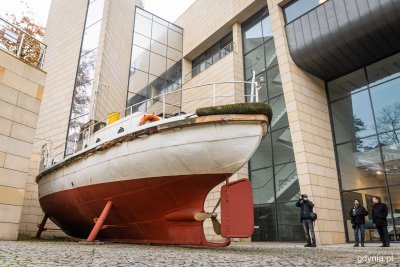 Niecka przy budynku Muzeum Marynarki Wojennej w Gdyni. Łódź na lądzie. W tle ludzie fotografujący łódź.