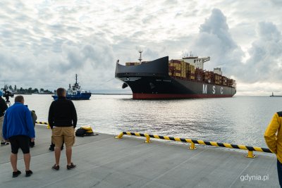 Ostroga Pilotowa, ludzie na nabrzezu, widoczne główki portu i wpływający kontenerowiec