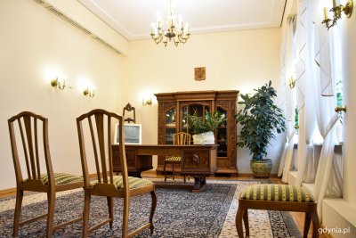 Pomieszczenie w Urzędzie Stanu Cywilnego. Na pierwszym planie dwa drewniane krzesła. Na podłodze wzorzysty dywan. W tle drewniane meble.