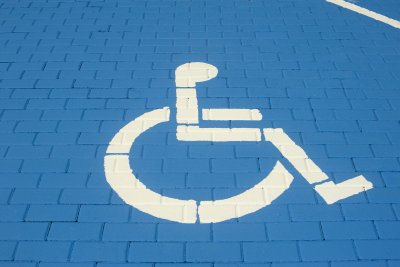 Parking z płaskiej kostki brukowej z wymalowanym niebieskim polem oraz symbolem wózka inwalidzkiego.