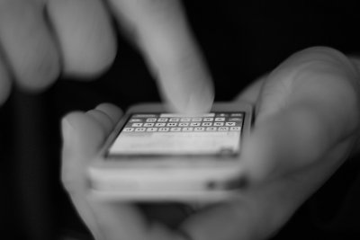 Ręce dorosłej osoby, smartfon w rękach. Palcem osoba wpisuje tekst z wyświetlanej klawiatury