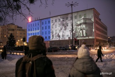 Na pierwszym planie widać dwoje ludzi. Para ogląda pokaz audiowizualny wyświetlany na fasadzie budynku Urzędu Miasta Gdyni.