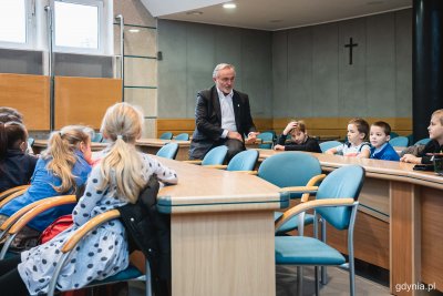 Sala obrad Rady Miasta Gdyni. Prezydent Wojciech Szczurek opiera się o stół, przy ławkach siedzą dzieci.
