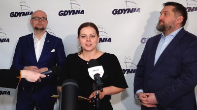 Ściana z logotypami Gdyni, stoją Bartłomiej Austen, Aleksandra Kosiorek i Tadeusz Szemiot, na środku mikrofon