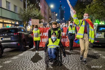 Pochód manifestujących idzie ulicą Gdyni z transparentami, na czele mężczyzna na wózku inwalidzkim