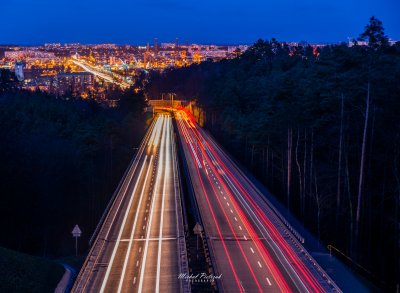 Fragment trasy Kwiatkowskiego z lasem, od strony Leszczynek. Noc. Widoczne światła samochodów