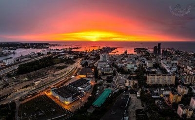 Zdjęcie lotnicze Portu Gdynia i części Śródmieścia. Zachód słońca, pomarańczowe niebo. Widoczny fragment morza.