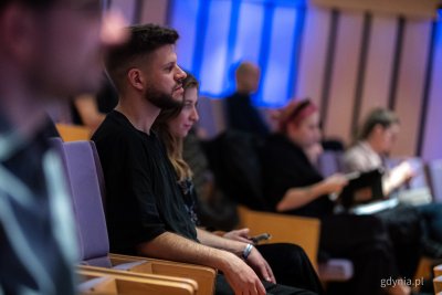 Sala konferencyjna w PPNT Gdynia, mężczyzna i kobieta siedzą na widowni, w tle inni ludzie