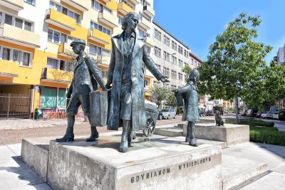 Na zdjęciu Michała Puszczewicza pomnik Gdynian Wysiedlonych przedstawiający matkę z dwojgiem dzieci idącą z walizką. Na ich twarzach widać smutek. Drugą część pominika stanowi pies, który nie może z nimi pójść. W tle ulica Starowiejska w stronę ul. 3 Maja.