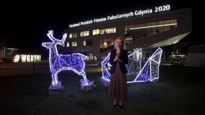 Prowadząca otwarcie FPFF stoi na placu Grunwaldzkim, obok świąteczne iluminacje, w tle Gdyńskie Centrum Filmowe z podświetloną nazwą festiwalu