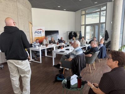 Na zdjęciu stojący tyłem do aparatu urzędnik prowadzi prezentacje dla osób zebranych przy stole roboczym w kształcie litery 