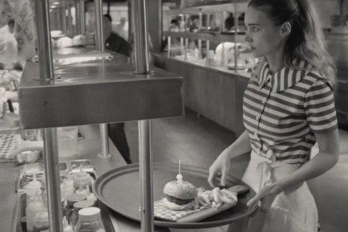 Kadr z filmu „Apetyt na więcej. La Cocina”. Czarno-białe zdjęcie. Amerykański bar, kucharz patrzy na kelnerkę z hamburgerem na tacy.