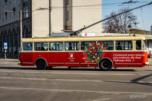 Ulica w Gdyni, czerwony, zabytkowy trolejbus oklejony na Dzień Kobiet