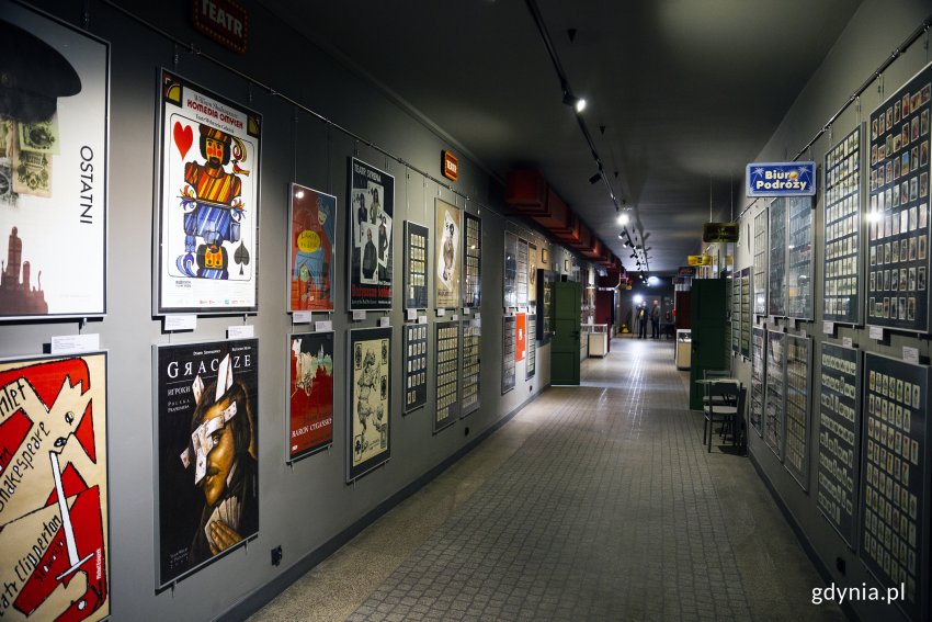 Hol Muzeum Kart do Gry. Na ścianie po prawej stronie wiszą gabloty z kolekcjami kart, po lewej stronie - antyramy z plakatami z motywami karcianymi.