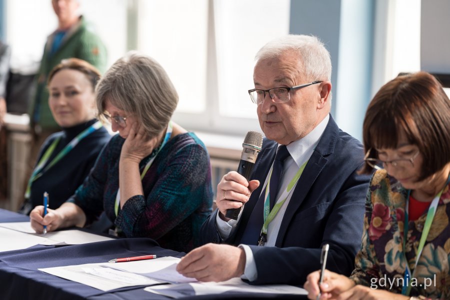 Jury siedzące przy biurku, mężczyzna mówi prze mikrofon