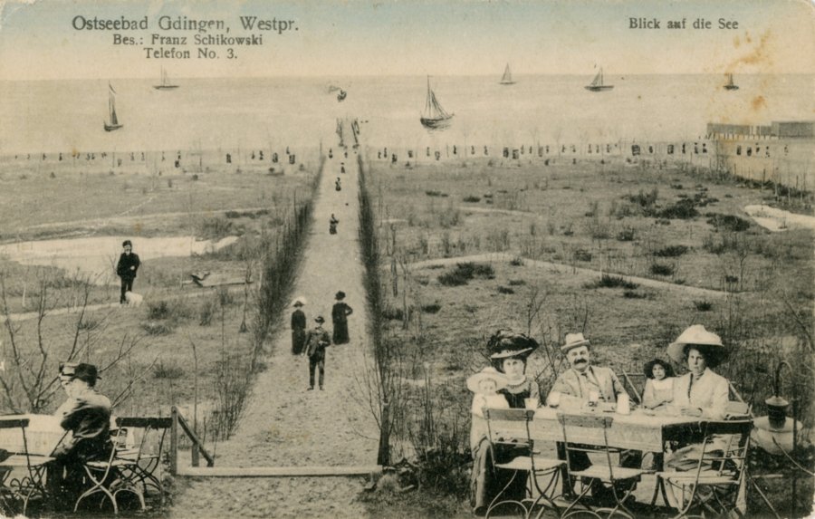 Stara pocztówka Gdyni. Droga wiodaca do morza, przy niej ludzie przy stolikach.
