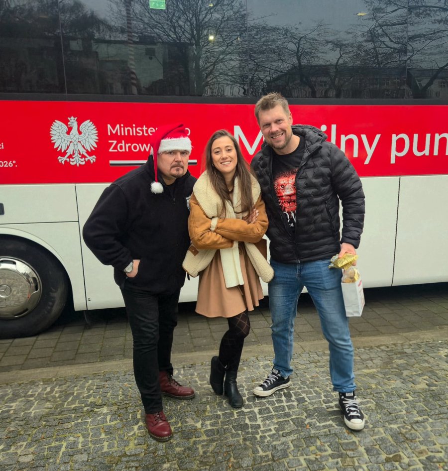 Dwójka młodych ludzi i mężczyzna w czapce świętego Mikołaja na tle ambulansu 