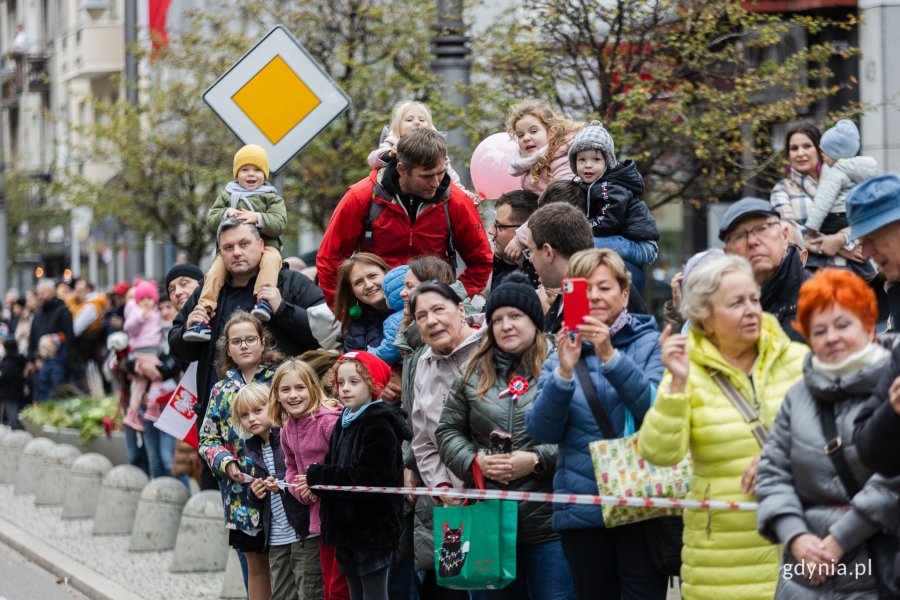 Osoby przyglądające się paradzie z okazji Narodowego Święta Niepodległości. Kobieta na pierwszym planie trzyma w ręku biało-czerwoną flagę z symbolem Polski Walczącej// fot. Karol Stańczak