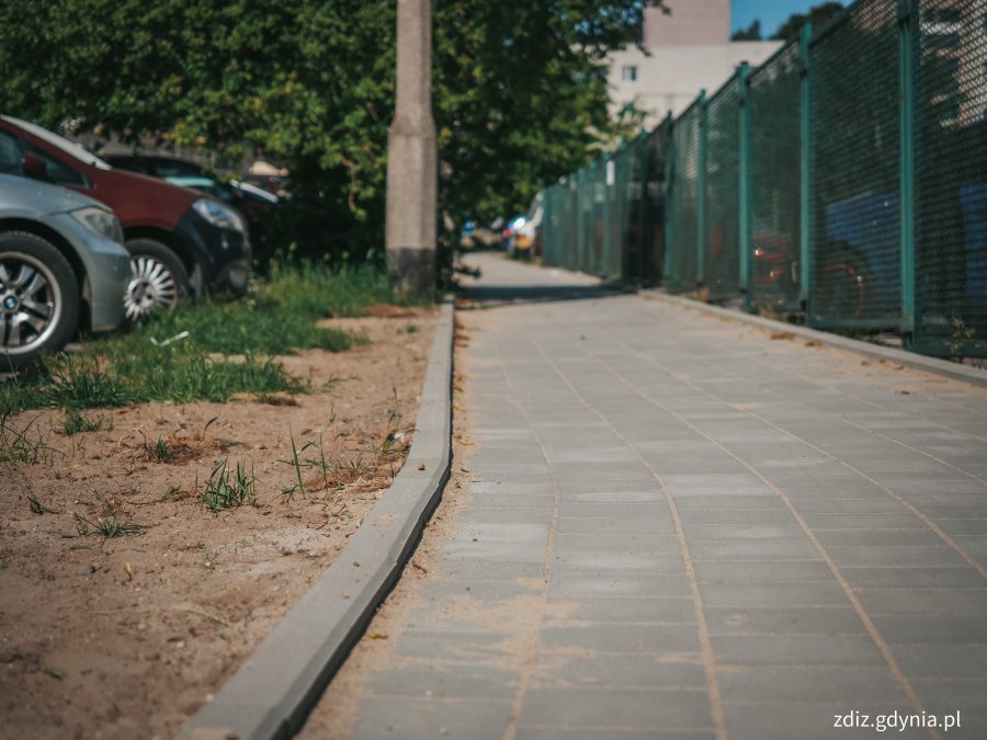 nowy chodnik na ul. Makuszyńskiego 17, w tle widoczne ogrodzenie, zaparkowane pojazdy